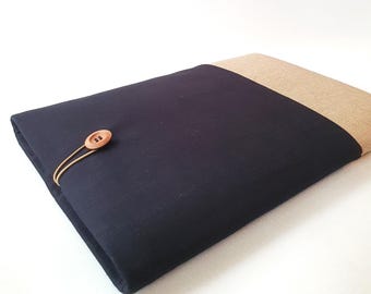 May include: A navy blue and tan fabric sleeve with a wooden button closure. The sleeve is rectangular and appears to be made of a soft material. The button is attached with a thin, tan cord.