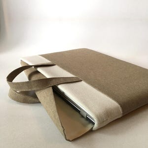 May include: A beige and white laptop sleeve with a handle. The sleeve is made of a textured fabric and has a flap that closes with a zipper.