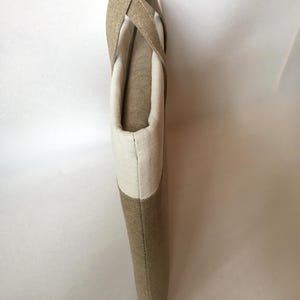 May include: A beige and white tote bag with a long strap. The bag is made of a woven fabric and has a simple design.
