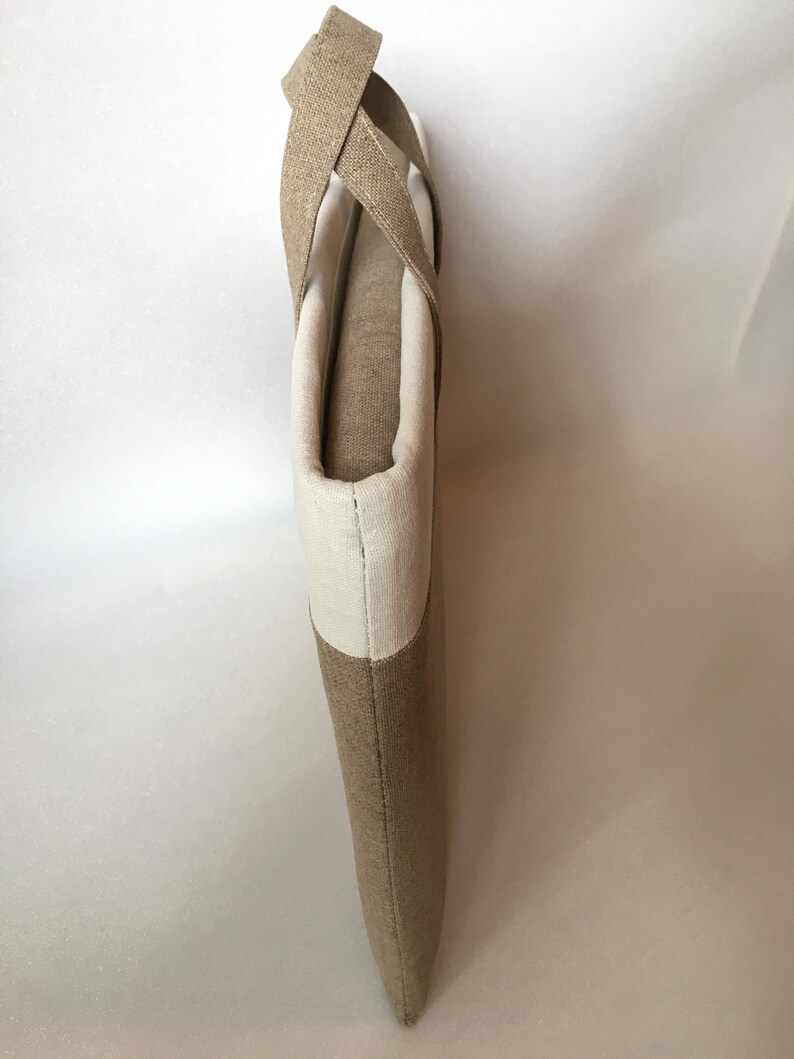 May include: A beige and white tote bag with a long strap. The bag is made of a woven fabric and has a simple design.