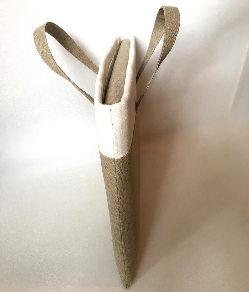 May include: A beige and white linen tote bag with two handles. The bag is made of a natural fabric and has a simple, elegant design.