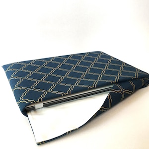 Könnte beinhalten: Eine dunkelblaue Laptoptasche mit einem goldenen geometrischen Muster. Die Tasche ist geöffnet und ein Laptop befindet sich im Inneren.