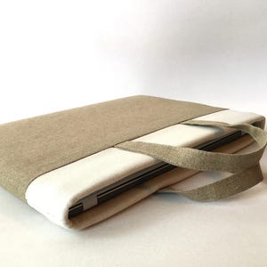 May include: A beige linen laptop sleeve with a white lining and a matching linen handle. The sleeve is closed and a laptop is visible inside.