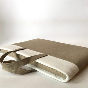 May include: A beige linen laptop sleeve with a white linen panel and a brown linen handle.