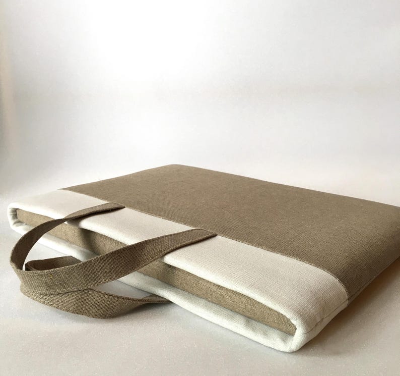 May include: A beige linen laptop sleeve with a white linen panel and a brown linen handle.