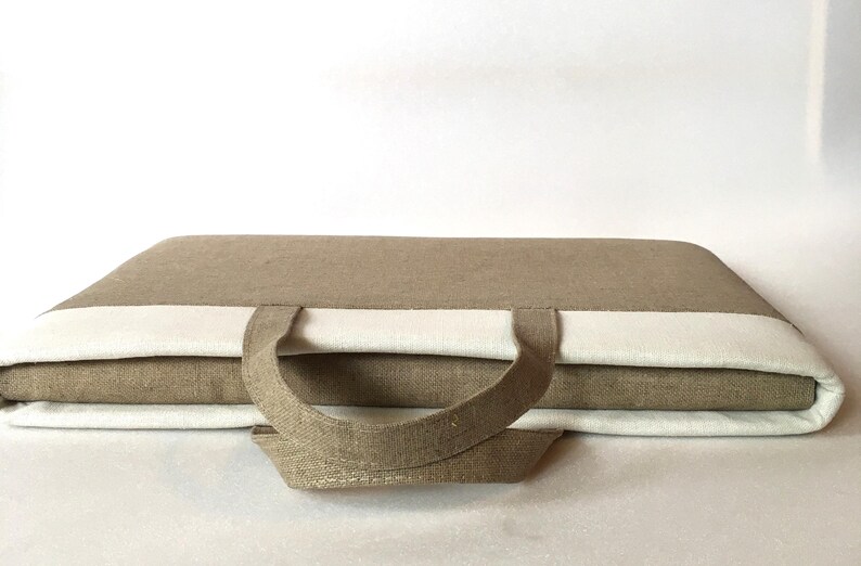 May include: A brown linen laptop bag with white trim and a top handle. The bag is closed and the handle is folded down.