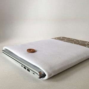 May include: White laptop sleeve with a brown button and a patterned fabric lining. The sleeve is made of a soft, durable material and is designed to protect your laptop from scratches and bumps.