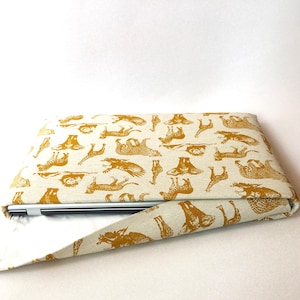 Könnte beinhalten: Eine beige Laptoptasche mit einem goldenen Tierdruckdesign. Die Tasche ist über einen Laptop gefaltet, so dass das Innenfutter sichtbar ist.