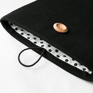 May include: Black laptop sleeve with a white polka dot lining and a wooden button closure. The sleeve has a black elastic handle.