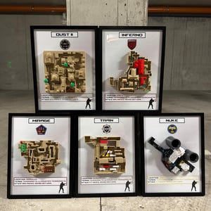 Könnte beinhalten: Fünf gerahmte Karten von Videospiel-Levels, darunter "Dust II", "Inferno", "Mirage", "Train" und "Nuke". Jede Karte ist mit Bausteinen konstruiert und verfügt über detaillierte Layouts und farbcodierte Bereiche. Die Rahmen sind schwarz.