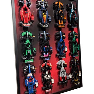 Può includere: Un'esposizione incorniciata con dodici auto da corsa in miniatura di vari colori, tra cui rosso, blu, nero e verde. Ogni auto è montata su uno sfondo rosso all'interno di una cornice nera. Alcune auto hanno loghi di sponsor.