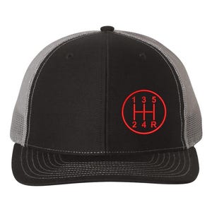 May include: A black and gray trucker hat with a red embroidered gear shift pattern. The pattern includes the numbers 1, 3, 5, 2, 4, and R.