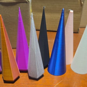 May include: Eight different colored, 3D printed cones. The cones are made of plastic and are in various shades of purple, orange, pink, gray, blue, and white.