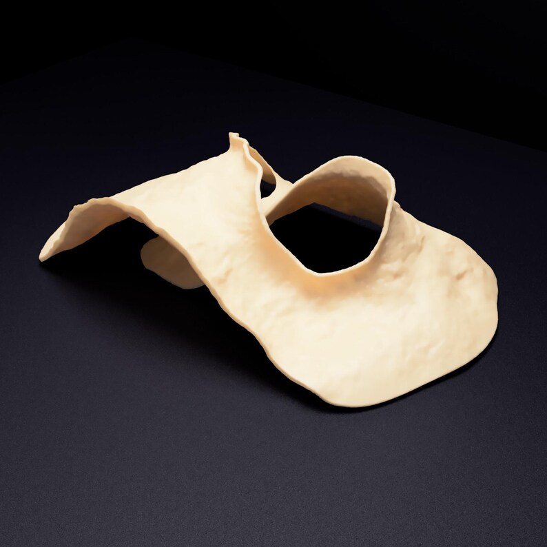 Op de afbeelding: Een cr&egrave;mekleurig, sculpturaal object met een onregelmatige, golvende vorm en een glad, mat oppervlak. Het stuk heeft een centrale ronde opening en gebogen, vloeiende randen die een dynamische, driedimensionale vorm cre&euml;ren.