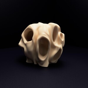 May include: A cream-coloured, spherical sculpture featuring multiple irregular, hollowed-out openings across its surface. The object has a smooth, matte finish with organic, undulating contours that create a complex, porous, and three-dimensional form.