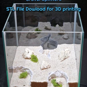 May include: A clear glass aquarium with white sand and several white 3D printed structures. The structures are designed to create barriers for gravel in an aquarium. The text "Gravel Splitters" and "STL File Download for 3D printing" is visible at the top of the image.