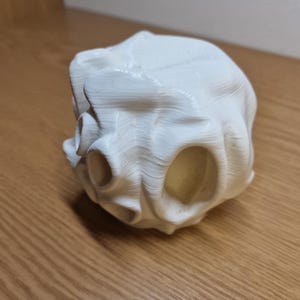 A side view of a white 3D-printed aquarium cave with smooth curves and multiple oval openings. Placed on a wooden surface, the design showcases an organic, flowing structure ideal for fish to explore and hide.