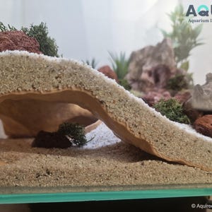 Close-up view of the Riptide Aquarium Cave STL file in a natural aquarium landscape, highlighting its textured sandy exterior and spacious hideout area for aquatic pets. Designed for 3D printing.
