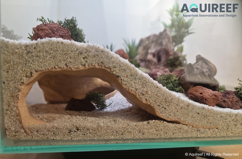 Close-up view of the Riptide Aquarium Cave STL file in a natural aquarium landscape, highlighting its textured sandy exterior and spacious hideout area for aquatic pets. Designed for 3D printing.