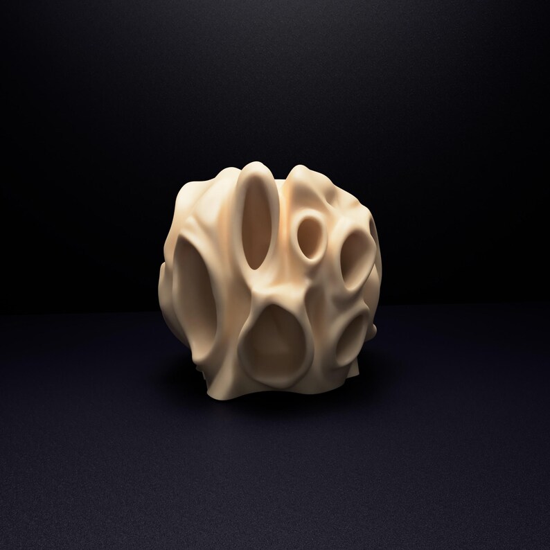 May include: A cream-coloured, spherical object with a smooth, matte surface featuring multiple irregular, hollowed-out openings of varying sizes. The structure has a porous, organic appearance with rounded edges and deep, recessed cavities throughout.
