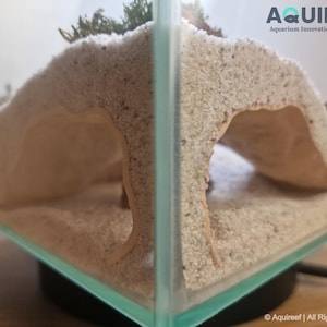 Corner view of the Riptide Aquarium Cave STL file in an aquarium setup, highlighting dual entrances, sandy texture, and compatibility with fish or reptiles. Designed for 3D printing and tank decoration.