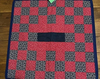 May include: A handmade quilt with a checkerboard pattern of red floral fabric and black and white floral fabric squares. A solid navy blue rectangle is sewn in the center. The quilt is bordered with navy blue fabric.