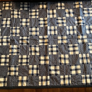 May include: A handmade quilt with a patchwork design. The quilt features alternating squares of navy blue and white plaid, navy blue with white polka dots, and solid navy blue fabric. The quilt is bordered with a dark blue fabric.
