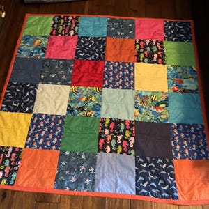 May include: A patchwork quilt with a variety of colorful squares. The squares feature solid colors like pink, green, and orange, and patterned fabrics with seahorses, fish, and dolphins. The quilt is bordered with a solid orange fabric.