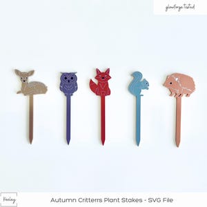 May include: Five wooden plant stakes with animal silhouettes. The stakes are painted in different colors: gold, purple, red, blue, and pink. The animals are a deer, an owl, a fox, a squirrel, and a hedgehog. The stakes are labeled "Autumn Critters Plant Stakes - SVG File".