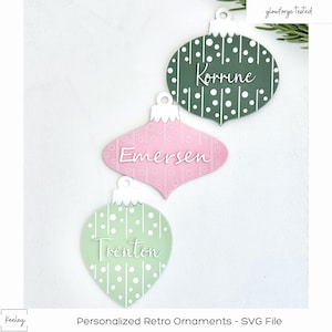 May include: Three personalised retro Christmas baubles with white polka dots and stripes on a green and pink background. The baubles are labelled "Korrine", "Emerson", and "Trenton".