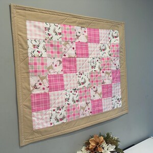 Puede incluir: Una colcha de retazos rosa y blanca con un borde marrón. La colcha presenta un estampado de ciervo y flores.