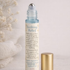 May include: A blue glass roller bottle with a silver rollerball and a gold cap. The bottle is labeled "Teething Relief" and lists organic ingredients. The product is designed for soothing support and comfort during teething.