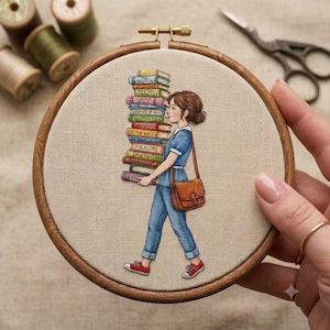 May include: An embroidery hoop containing a fabric panel with a stitched illustration of a person carrying a tall stack of colorful books. The person wears a blue shirt, blue jeans, and red sneakers, with a brown leather-style satchel bag.