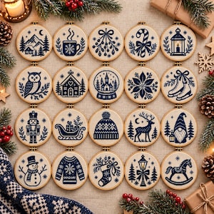 May include: A collection of twenty circular embroidery hoops featuring dark blue cross-stitch designs on a light fabric. The patterns include winter themes such as a mountain landscape, a mug, mistletoe, a candy cane, a lantern, an owl, a house, a snow globe, a poinsettia, ice skates, a nutcracker, a sleigh, a beanie, a deer, a gnome, a snowman, a sweater, a stocking, a street lamp, and a rocking horse.