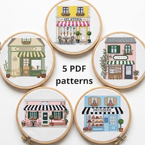 以下が含まれることがあります： 5つの円形刺繍枠に、黄色いジェラート店、緑の本屋、ピンクのコーヒーショップ、ピンクのカフェ、青いパティスリーのクロスステッチパターンが収められています。中央には「5 PDF patterns」というテキストが配置されています。