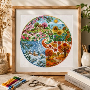 Peut inclure: Une broderie au point de croix encadrée représentant les quatre saisons dans un motif en spirale circulaire. L'œuvre présente des fleurs printanières, des tournesols estivaux, un feuillage automnal avec des citrouilles et un paysage hivernal.