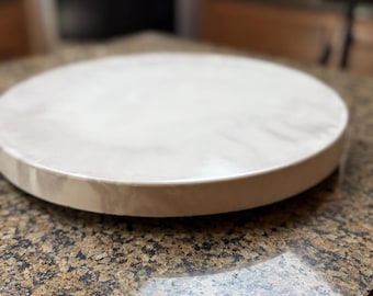 May include: A round, off-white wooden serving tray with a slightly raised edge. The tray is set on a granite countertop. The tray is approximately 12 inches in diameter, suitable for serving appetizers or desserts.