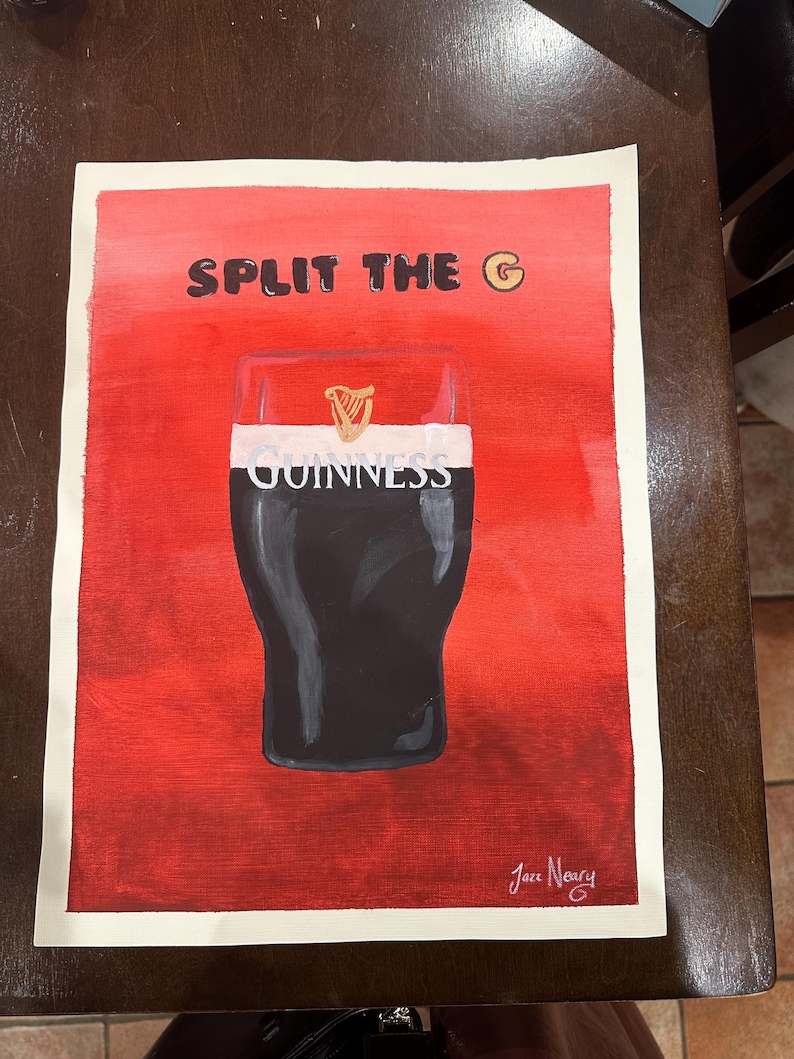 以下が含まれることがあります： 「SPLIT THE G」という文字が書かれたギネスビールのグラスを描いた絵画。背景は赤で、グラスは白い表面の上に置かれている。絵画には「Jace Neary」という署名がある。