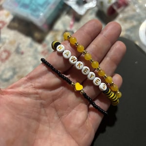 May include: Three bracelets with black and yellow beads. One bracelet has the word "HAWKEYES" spelled out in white beads with gold lettering. Another bracelet has a small yellow heart charm.