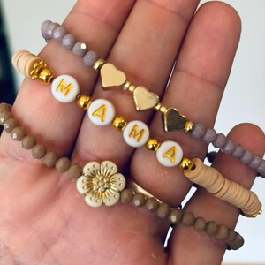 Könnte beinhalten: Ein Set aus vier Armbändern mit braunen und violetten Perlen. Die Armbänder haben einen Blumenanhänger und Buchstabenperlen, die "MAMA" buchstabieren.