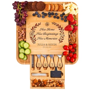 May include: A bamboo charcuterie board with a variety of snacks, including grapes, cheese, cookies, and nuts. The board is engraved with "New Home New Beginnings New Memories" and the names "JULIA & KEVIN" with the date "EST. JULY, 2025". Includes cheese knives.