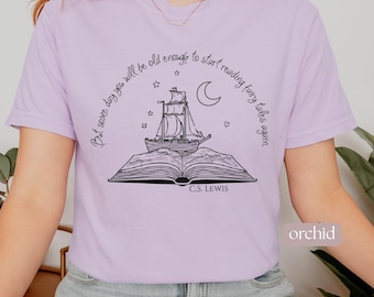 May include: Orchid-colored t-shirt with a black illustration of a ship sailing out of an open book, with stars and a crescent moon. The text reads "But some day you will be old enough to start reading fairy tales again" and "C.S. Lewis".