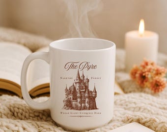May include: White ceramic mug with the text "The Pyre" and a detailed illustration of a castle. The mug also features the text "Narethe Forest" and "Where Light Conquers Dark". Steam rises from the mug, suggesting a warm beverage.