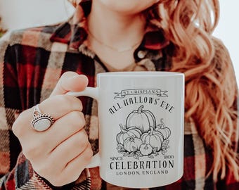 May include: White ceramic mug with a black and white pumpkin illustration and the text "ALL HALLOWS EVE CELEBRATION LONDON, ENGLAND SINCE 1800". The mug is held by a person wearing a red and black plaid shirt.
