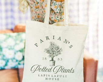 Puede incluir: Bolso tote de color crema con texto negro e ilustración de una planta en maceta. El texto dice "PARIAN'S 1883 Potted Plants LAPIS LAZULI HOUSE". El bolso tiene dos asas.