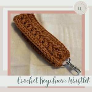 May include: A handcrafted, rust-colored crochet keychain wristlet. The wristlet features a textured, braided design and a silver-colored clasp. The text "Crochet Keychain Wristlet" is displayed at the bottom of the image.