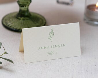 May include: A white place card with a green sprig design and the text "ANNA JENSEN Table 3".