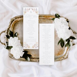 May include: A silver serving tray holds two wedding ceremony programs with floral accents and text. White flowers and greenery are arranged around the tray. The programs feature the names of the couple and the date.