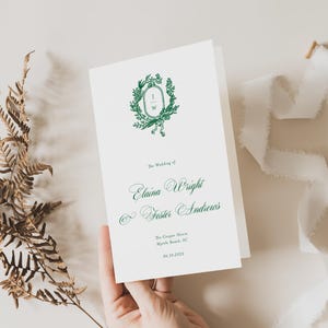 May include: A white wedding program with green calligraphy. The program features the names "Elaina Wright & Foster Andrews" and the date "May 10, 2023".