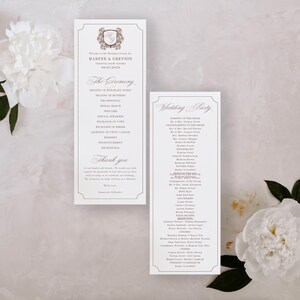 May include: Two white wedding ceremony programs with elegant script and a decorative border. The programs are placed on a light background with white flowers and green leaves. The text includes the names "Harper & Greyson" and "The Ceremony."